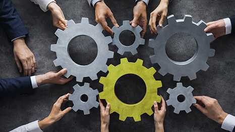 Mehrere Hände fügen Zahnräder zusammen – Teamarbeit